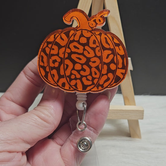 Pumpkin badge reel made with orange mirrored acrylic. The image is engraved into the acrylic and the back of the badge is covered with white acrylic. 