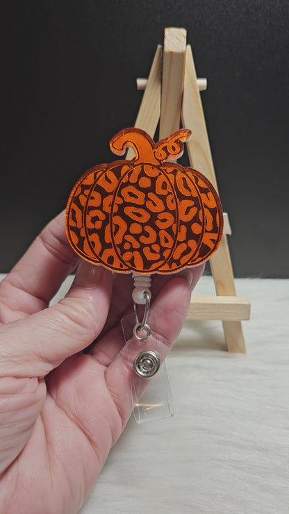 Pumpkin badge reel made with orange mirrored acrylic. The image is engraved into the acrylic and the back of the badge is covered with white acrylic. 